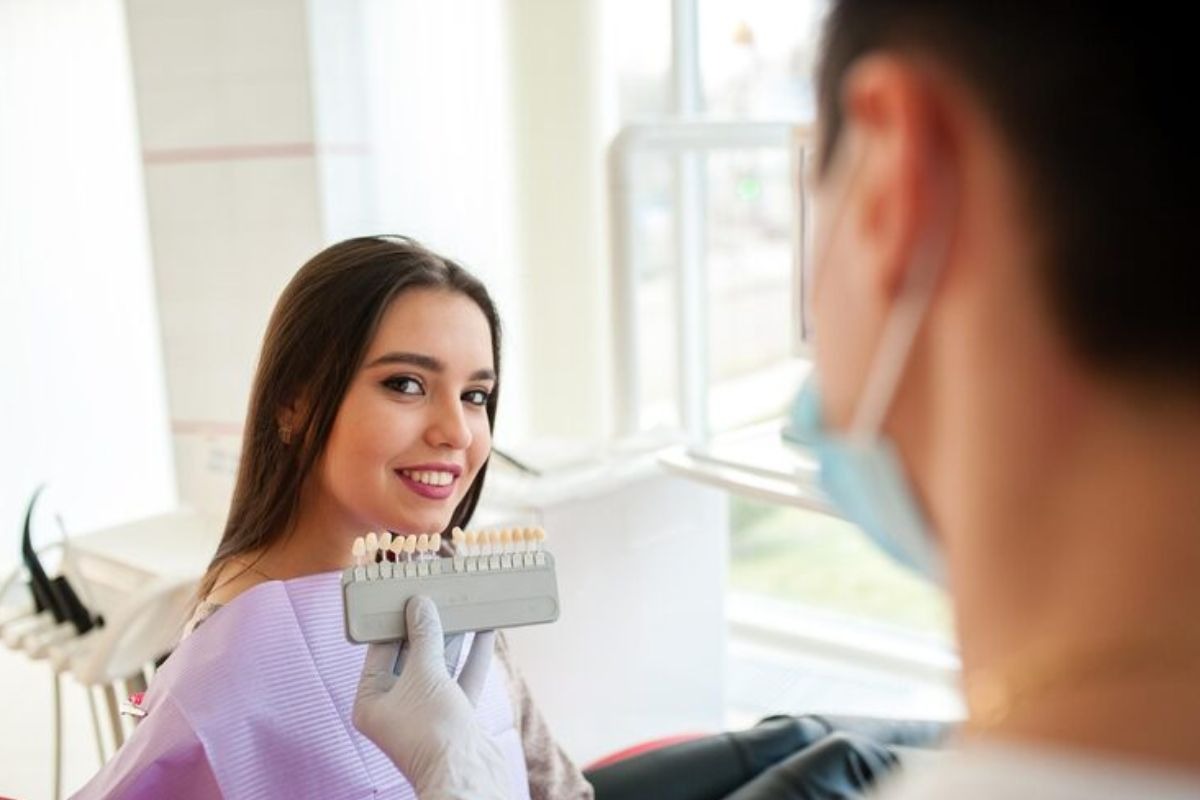 woman at a dental clinic comparing dental crown shades with a dentist to match her natural teeth.